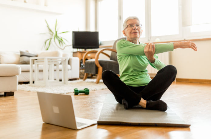 Senior woman exercising at home using an online trainer service.
