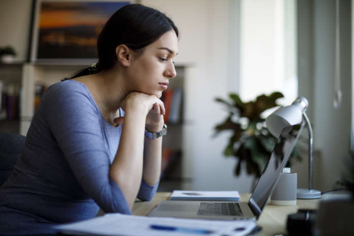 Worried young woman working on laptop at home