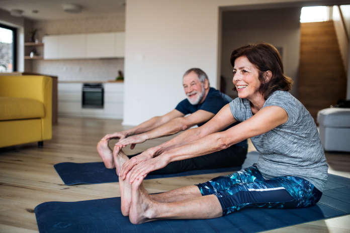 A happy senior couple indoors at home, doing exercise on the floor.