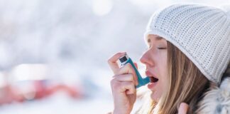 A woman wearing a woolly hat and warm coat using an asthma inhaler