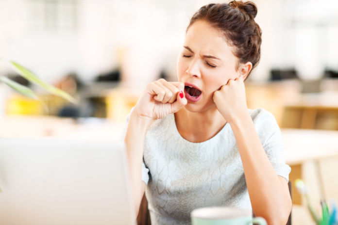 Tired female entrepreneur yawning in office.