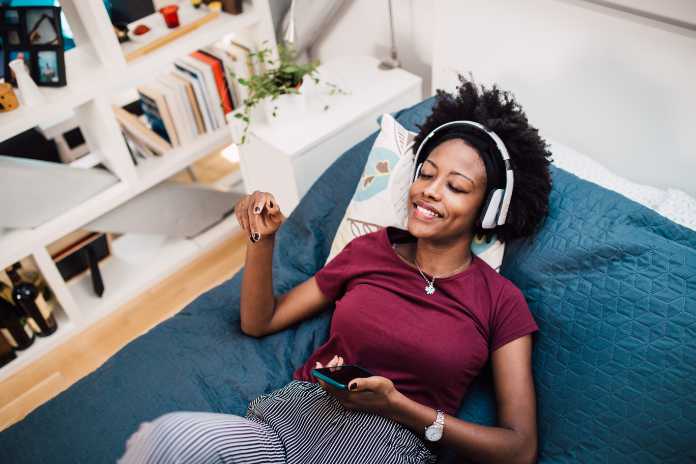 Beautiful African-American woman enjoying in her bed and listening to the music.