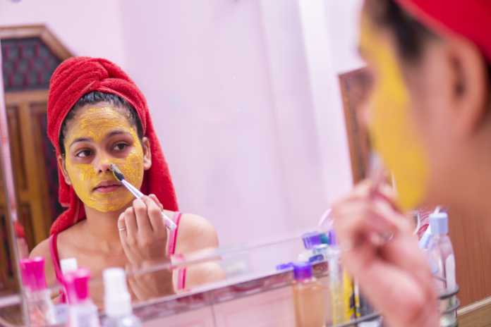 girl applying Gram flour (Besan) turmeric yellow face mask on face through brush. 