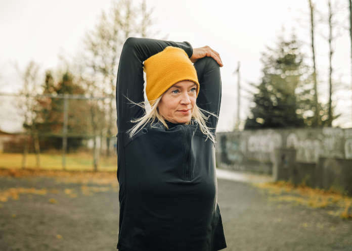 Jogger doing arm stretches in winter morning to improve winter wellbeing