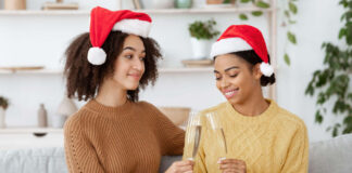 Stress-free ChristmasBlack lesbian couple wearing Santa hats, clinking champagne glasses while sat on the sofa