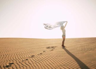 Standing woman against the sun on a desert dune