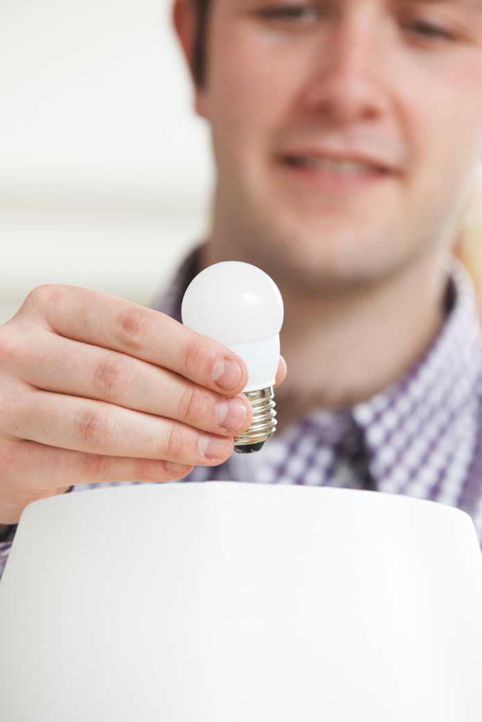 Man Putting Low Energy LED Light bulb Into Lamp At Home
