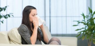 House allergies: Woman sitting on sofa at home and sneezing