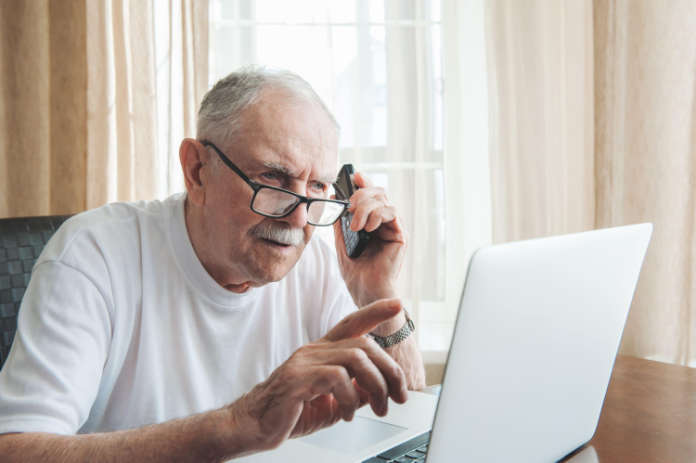 male senior gray hair working laptop interior. A gray-haired man of 87 years old speaks on the phone while working on a computer.