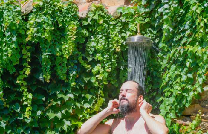 Bearded hipster man taking an outdoor shower in a garden with plants